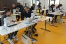Mehrere Studierende sitzen an Tischen mit Nähmaschinen