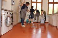 Drei Studierende notieren im Hauswirtschaftsraum Unterrichtsergebnisse, eine Studierende testet einen Wischmob.
