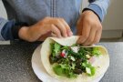 Hände falten einen Wrap mit Salat und Gemüse