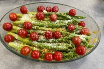 Gläserne Auflaufform mit grünem Spargel, Cocktailtomaten und Bröseln