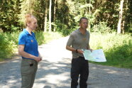 Auf einem Waldweg stehen eine Frau und ein Mann mit einer Karte.