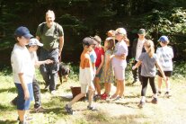 EIn Gruppe Kinder und ein Mann mit Hund stehen in einer Waldlichtung.