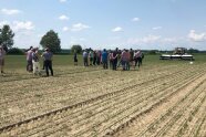 Menschen beobachten auf einem Feld eine Spritze bei der Arbeit.