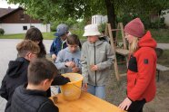 Kinder und eine Erwachsene stehen an einm Tisch und füllen Erde in kleine Pflanztöpfchen.
