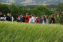 Kinder und Erlebnisbäuerin Stephanie Stahl stehen in einem grünen Gerstenfeld.