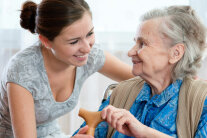 Pflegerin hilft älterer Frau mit Gehstock 